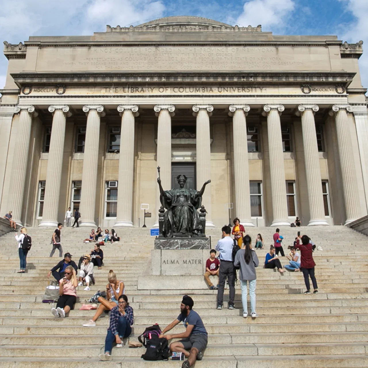 People walking and sitting on the steps of Low Library in the summer.