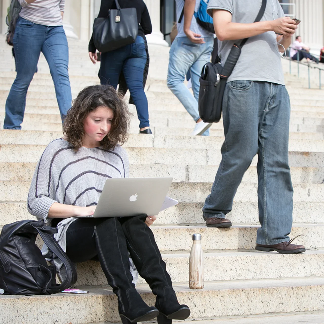 A woman works on her laptop on campus.