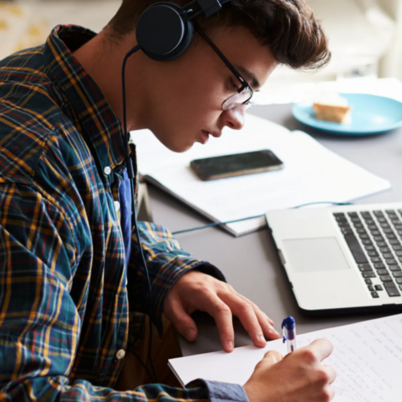 A student taking notes at a laptop with headphones on.